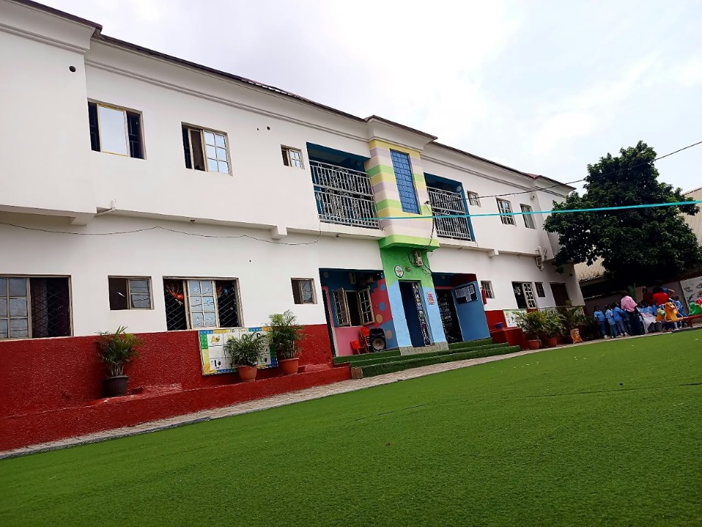 The white school building, red lower wall, painted entrance, and green front field